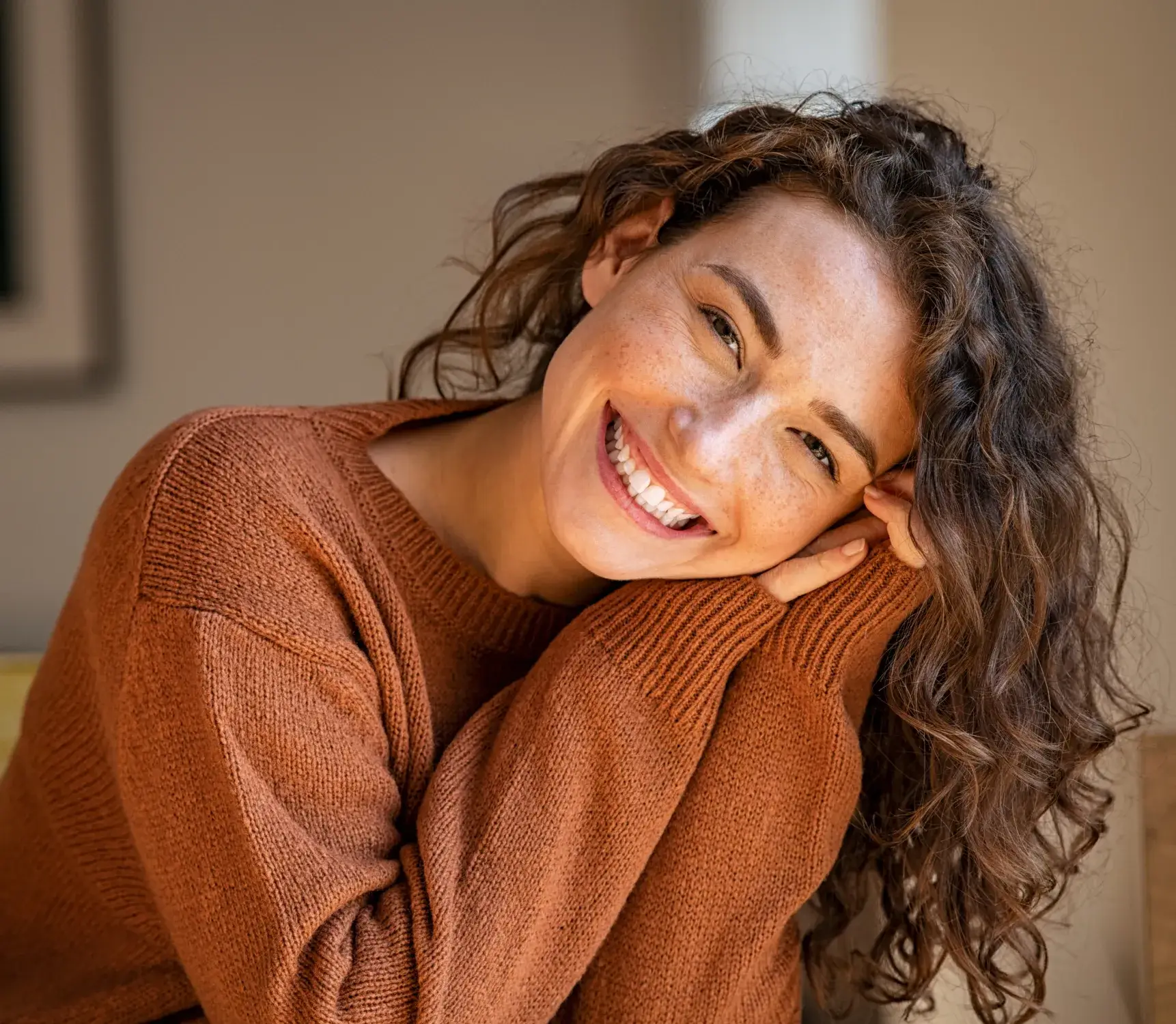 a smiling woman in a brown sweater sitting on a couch